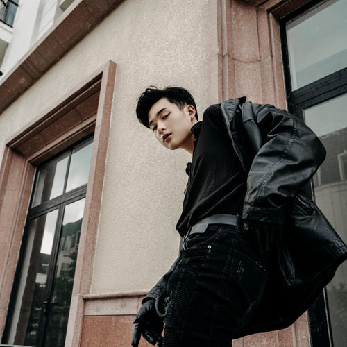 asian man standing on the street wearing an all black outfit, black pants, black shirt, and black jacket